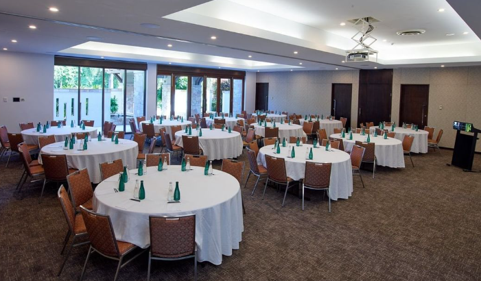 A view of a conference room that has numerous round tables which are covered
in white drapes. The tables are surrounded by chairs and there are water
bottles on them.